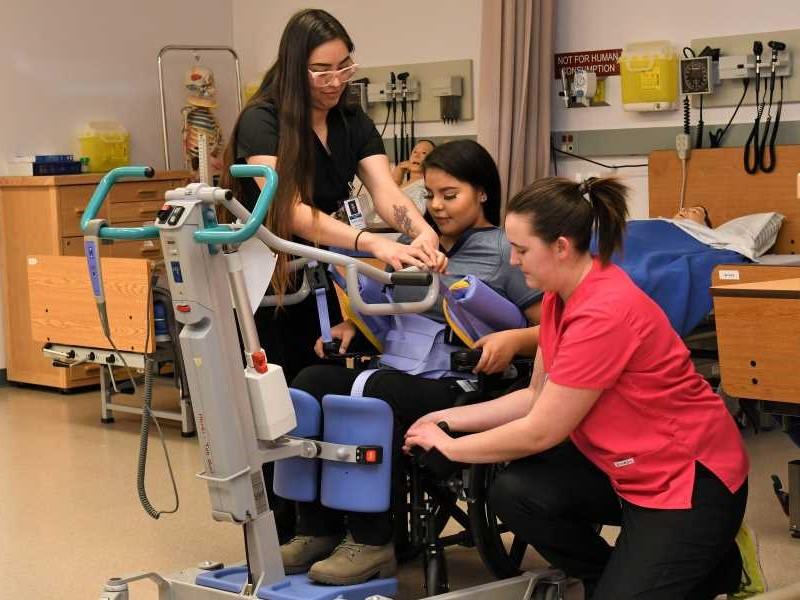Putting a classmate into a lift as part of a health care aide lab.